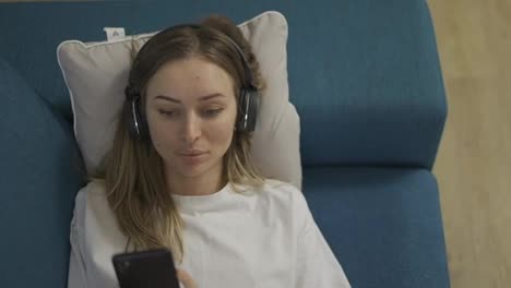 Top-view-serene-caucasian-blonde-woman-lying-on-sofa-pillow-listening-to-music-in-headphones