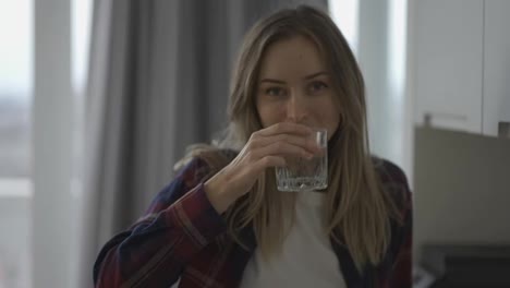 Woman-drinking-water-on-domestic-kitchen,-looking-to-the-camera