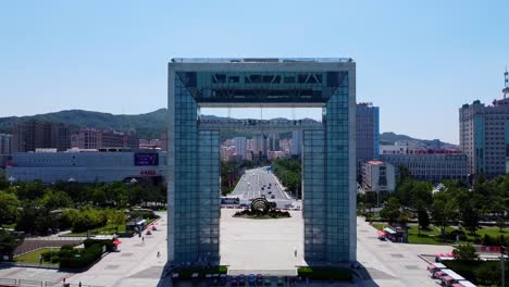 Aerial-dolly-reverse-shot-of-the-mighty-xingfu-gate-in-xingfu-park-in-weihai-city,-china-overlooking-the-busy-road-with-traffic-and-people-visiting-the-park-on-a-summer-day