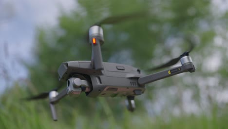 Close-up-shot-of-a-hovering-drone-from-a-low-angle,-with-trees-and-grasses-in-the-background
