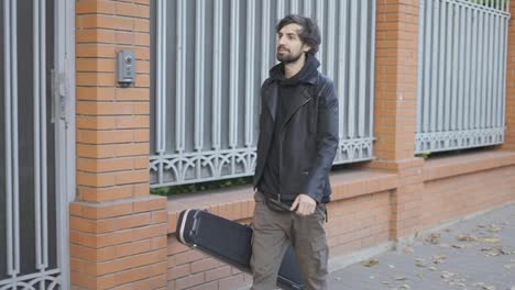 Happy-man-holding-a-guitar-case-while-walking