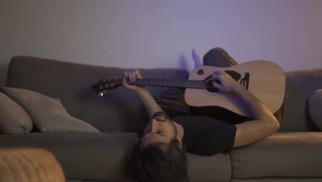 Sad-man-playing-guitar-while-lying-on-sofa
