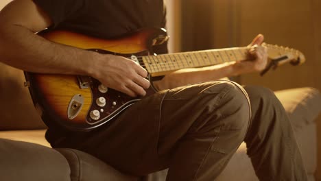 Man-plays-the-guitar-while-sitting-on-the-couch