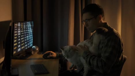 Young-guy-looking-at-screen-traiding-online-from-home-office-sit-with-cute-white-fluffy-cat