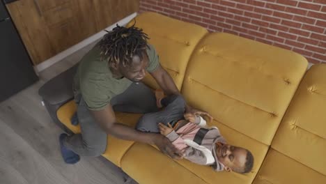 Afro-american-dad-playing-with-small-kid-boy-tickling,-cuddling-together-at-home
