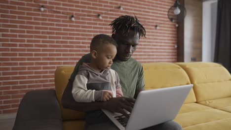 Young-african-american-dad-showing-website-explaining-device-work-sit-on-sofa