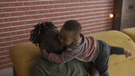 Afro-american-dad-playing-with-small-kid-boy-hugging,-cuddling-together-at-home