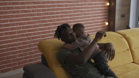 Afro-american-dad-with-his-son-hugging,-cuddling-together-at-home
