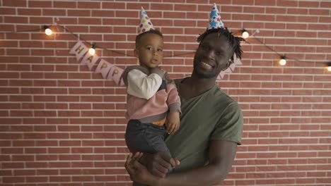 Portrait-of-cute-afro-american-boy-on-father's-arms-in-b-day-hats