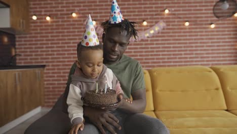 Der-Afroamerikanische-Vater-Hält-Seinen-Sohn-Und-Bläst-Drei-Kerzen-Auf-Den-Geburtstagskuchen
