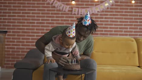 Carefree-father-holds-son---blowing-three-candles-on-birthday's-cake
