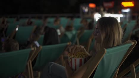 Woman-sits-on-a-comfy-lounger-eating-popcorn-at-summer-cinema