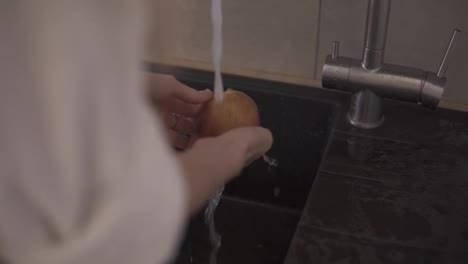 Woman-hands-washing-apple-in-the-kitchen-sink