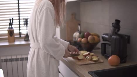 Woman-at-kitchen-cutting-apple-with-a-knife-on-a-wooden-cutting-board-to-make-juice