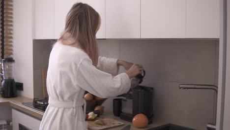 Woman-in-white-robe-making-apple-or-pear-juice-in-the-morning-using-juicer-at-kitchen