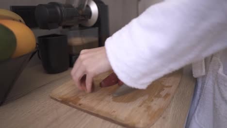 Unrecognizable-woman-at-kitchen-cutting-apple-with-a-knife-on-a-wooden-cutting-board-to-make-juice
