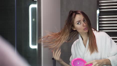 Pretty-woman-doing-long-hair-style-looking-at-mirror,-girl-brushing-hair-in-bathroom