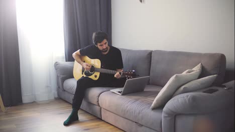 A-young-man-plays-the-guitar-through-a-video-call-on-a-laptop-or-practicing-at-home