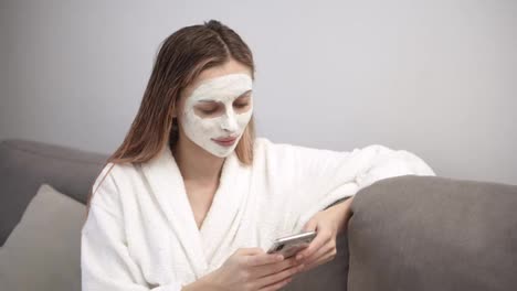 Mujer-Con-Máscara-Cosmética-Relajándose-En-El-Sofá-Y-Usando-El-Teléfono-Móvil