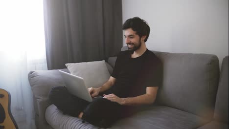 Hombre-Feliz-Relajándose-En-El-Sofá-Mientras-Realiza-Videollamadas-Usando-Una-Computadora-Portátil-En-Casa