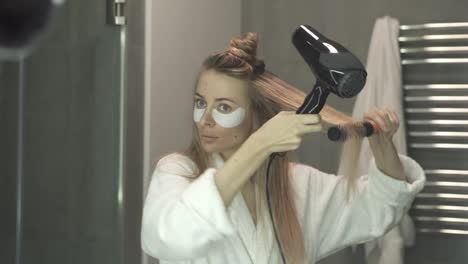 Woman-with-eye-patches-drying-her-hair-with-hair-dryer-and-brush