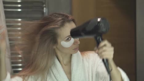 Confident-woman-looking-at-her-reflection-and-drying-her-hair-with-hair-dryer