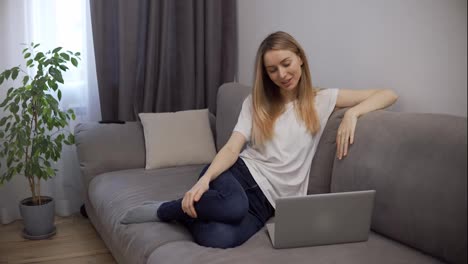 Mujer-Rubia-Relajándose-En-El-Sofá-Mientras-Realiza-Videollamadas-Usando-Una-Computadora-Portátil-En-Casa