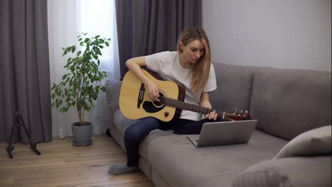 A-young-woman-plays-the-guitar-through-a-video-call-on-a-laptop