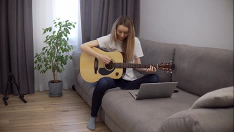 Portrait-of-a-woman-plays-the-guitar-through-a-video-call-on-a-laptop,-leaning-chords