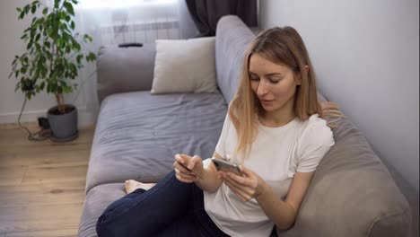 Blonde-woman-sitting-on-a-sofa,-pays-for-purchases-online-with-a-credit-card-and-phone-home