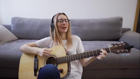 Woman-in-headphones-plays-the-guitar-at-her-home,-happily-having-fun-playing-guitar-and-singing