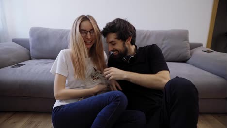 Beautiful-young-couple-with-their-cat-on-their-living-room-couch-talking-to-the-camera