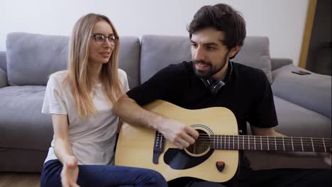 Mann-Mit-Kopfhörer-Spielt-Zu-Hause-Gitarre-Und-Singt-Fröhlich-Mit-Seiner-Freundin