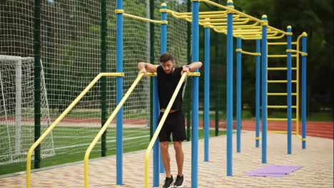 Muscular,-bearded-man-came-to-perform-push-ups-on-crossbar-outdoors-on-modern-stadium-with-equipment