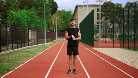 Fit,-bearded-man-standing-on-running-track-outdoors-on-modern-stadium-warming-up-his-wrists