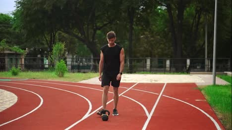 A-man-in-black-sportswear-with-a-beautiful-body-sculpture,-trains-with-weight.-Outdoors-close-to-the-stadium