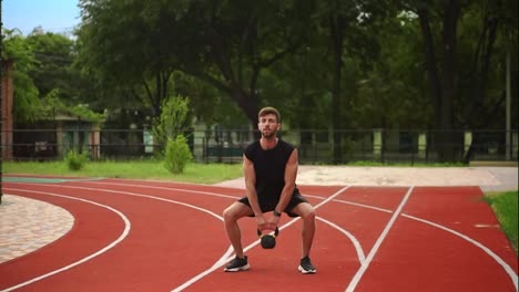 A-man-in-black-sportswear-trains-with-weight-bob-outdoors-close-to-the-stadium-on-the-racetrack