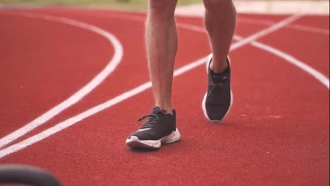 Close-up-footage-of-a-man's-legs-in-black-sneakers-comes-to-train-with-weight-bob-outdoors-on-the-racetrack