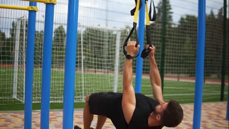 Caucasian-sportsman-doing-pull-ups-exercise-using-rubber-belt-to-force-strenth-of-workout-outdoors