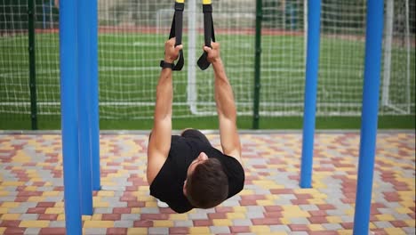 Caucasian-sportsman-doing-pull-ups-exercise-using-fit-belt-to-force-strenth-of-workout-outdoors