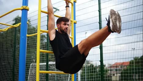 Athletic-man-training-core-muscles-with-leg-lift-on-vertical-ladder-rack-on-an-outdoors-gym-center