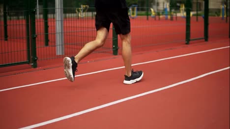 Close-up-of-male-legs,-an-athlete-is-running-on-race-track-in-athletics-stadium