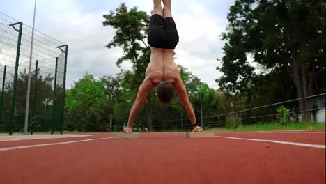 A-shirtless-athlete-is-standing-upside-down-leaning-on-special-racks-on-race-track-outdoors