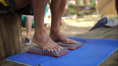Male-feet-stand-on-a-wooden-yoga-board-with-lot-of-metal-nails-pins-then-step-out-from-it-carefully