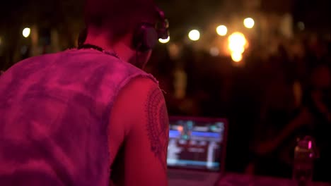 DJ-Arbeitet-Mit-Geräten,-Mischt-Musik-–-Leute-Tanzen,-Verschwommene-Aufnahmen-Einer-Feuershow-Im-Hintergrund