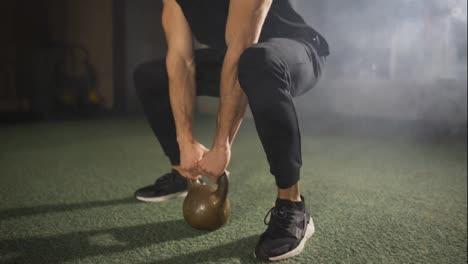 Man-working-out-with-kettlebell,-dark-foggy-gym