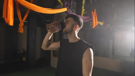 Hombre-Duro-Bebiendo-Agua-De-La-Botella-En-El-Gimnasio-Oscuro