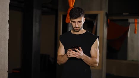 Young-man-use-phone-at-dark-gym
