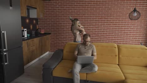 Mother-plays-with-her-son-at-home-while-their-father-busy-with-laptop-on-the-sofa