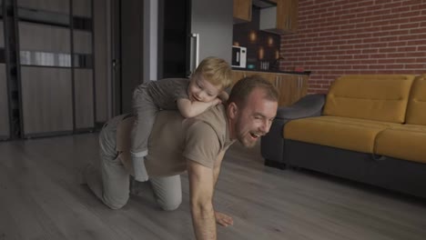 Father-playing-with-his-son,-riding-him-on-the-back-at-living-room